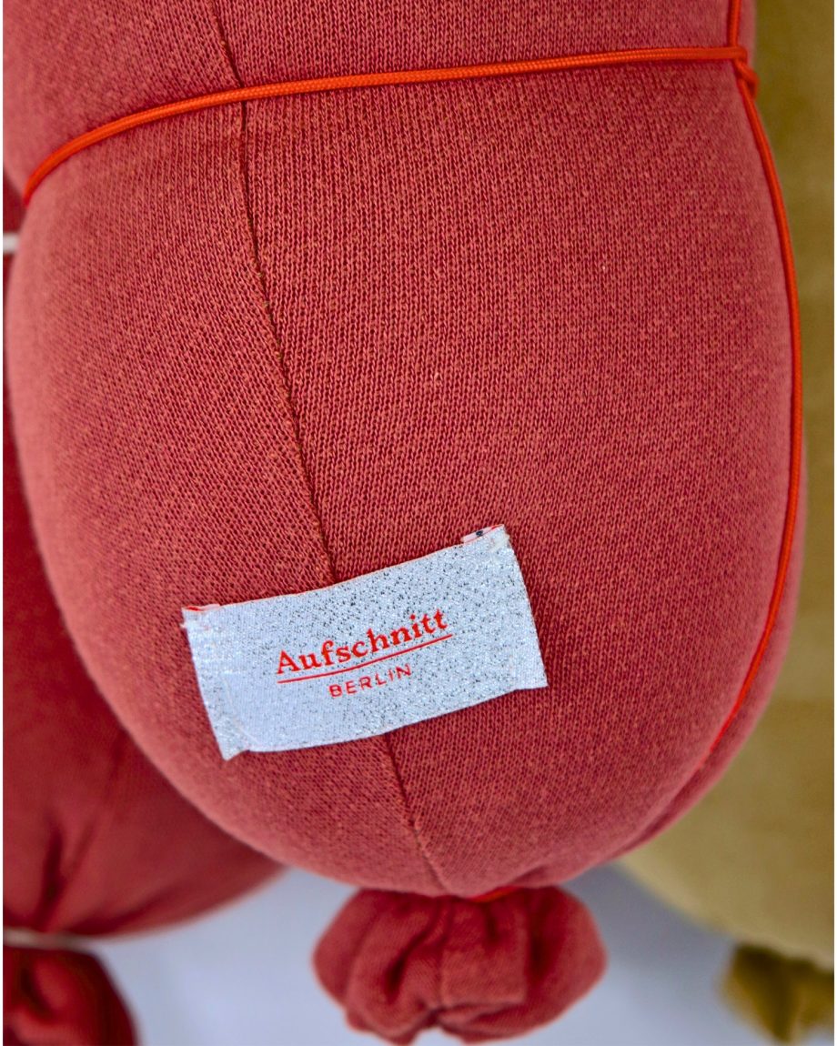 Gemütliches Reisekissen und Nackenkissen von Aufschnitt Berlin in Form eines Bockwurstkissen in orange für Reisen und unterwegs.